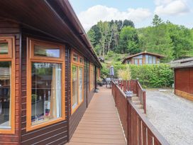 Wooden deck walkway with railings outside wooden cabins surrounded by trees and greenery at Pheasant's Nest Kirkstone 11 Limefitt Park near Windermere