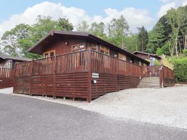 A wooden cabin with a fenced deck and stairs surrounded by trees at Pheasant's Nest Kirkstone 11 Limefitt Park near Windermere