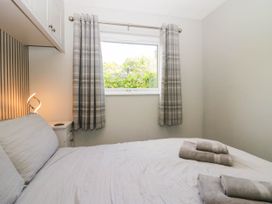 A bedroom with a bed, curtains, and a lamp at Badgers Hollow Lodge Grasmere 30, White Cross Bay near Windermere