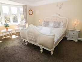 A bedroom with a large bed two bedside tables lamps a chair a round table with flowers and a bay window at Harbour Lights in Torquay
