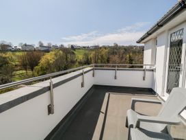 A balcony with a metal railing and plastic chairs overlooking green trees and houses at Harbour Lights in Torquay