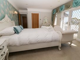 A bedroom with a bed and white bedding two blue pillows a white chair a dresser with a mirror and windows with blue curtains at Harbour Lights in Torquay
