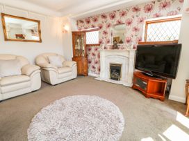 A living room with beige armchairs a fireplace a television on a wooden stand and floral wallpaper at Harbour Lights in Torquay