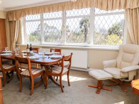 A dining room with a wooden table set for six and a cream armchair with ottoman at Harbour Lights in Torquay