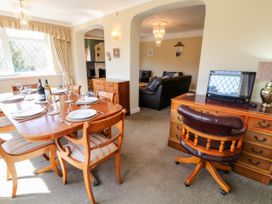 A dining area with a wooden table set with plates and wine bottles next to a living area with leather sofas and a desk with a computer at Harbour Lights in Torquay