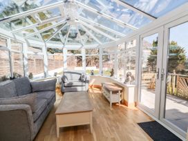 A conservatory with glass roof and windows containing grey sofas a wooden coffee table and side table at Harbour Lights in Torquay