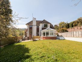 A garden with grass and a wooden bench in front of a house with a conservatory at Harbour Lights in Torquay