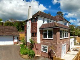 A two-story brick and white house with a tiled roof a chimney and an attached garage surrounded by trees and plants