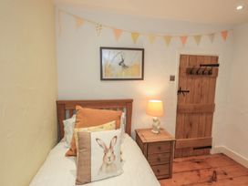 A bedroom with a bed, side table, lamp and decorations at Green Stile Cottage in Bowness-On-Windermere