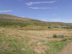 A grassy field with a rock and hills at Cwm in Capel Curig