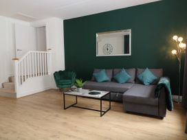 A living room with a grey corner sofa with blue cushions a green armchair a white staircase and a wooden floor at Sea Nest in Torquay