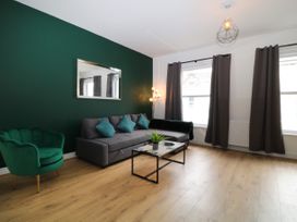A living room with a gray sofa green armchair coffee table and large windows with dark curtains at Sea Nest in Torquay