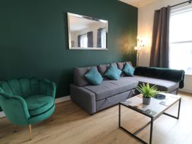 A living room with a gray sofa and blue cushions a green armchair a rectangular coffee table with a plant on it and a mirror on a green wall at Sea Nest in Torquay