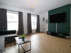 A living room with a gray sofa dark curtains a wall-mounted TV on a green accent wall and a coffee table with a plant at Sea Nest in Torquay