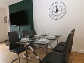 A dining room with a glass table set for six people black chairs a wall clock and a mounted television at Sea Nest in Torquay