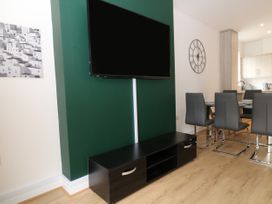 A dining area with a wall-mounted TV and black cabinet in a room with wooden flooring at Sea Nest in Torquay