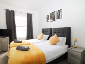 A bedroom with two single beds with yellow blankets and pillows a small bedside table with a lamp and a chest of drawers with a TV at Sea Nest in Torquay