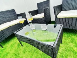 Outdoor seating area with black wicker chairs with cushions and a glass top table on green grass at Sea Nest in Torquay