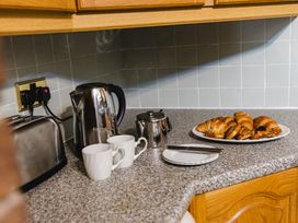 A kitchen counter with a kettle, toaster, mugs, teapot, and croissants at Fern Cottage in Akeld near Wooler