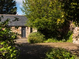 A stone building with a door and window surrounded by trees and bushes at Bramble Cottage in Akeld near Wooler
