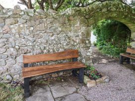 A garden with a stone wall and wooden benches at Catkin Cottage Akeld near Wooler