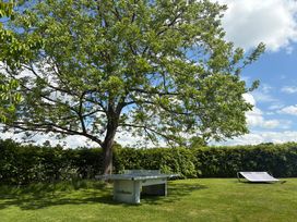 An outdoor scene with a ping pong table under a tree and a lounge chair on grass at The Stable House in Sherborne