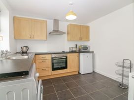 A kitchen with wooden cabinets a stove a microwave refrigerator a kettle and a metal shelf at Broadsands in Paignton