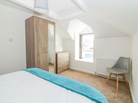 A bedroom with a bed with a blue blanket a wooden wardrobe with a mirror a wooden chest of drawers a grey chair and a window at Broadsands in Paignton