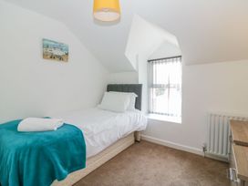 A small bedroom with a single bed with white bedding and a blue blanket a window with vertical blinds a radiator and a wooden chest of drawers at Broadsands in Paignton