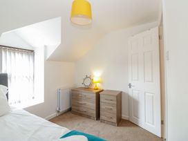 A bedroom with a bed a wooden dresser a wooden chest of drawers a small lamp and a round mirror at Broadsands in Paignton