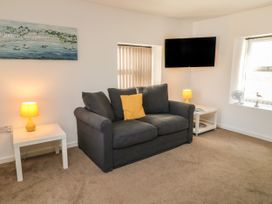 A sitting room with a dark grey sofa and yellow cushion between two white side tables with yellow lamps a wall-mounted TV and a window at Broadsands in Paignton