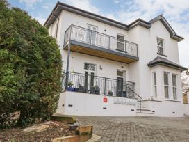 A white two-story building with balconies and black railings next to a large green bush at Apartment 4 10 Somers Court in Paignton