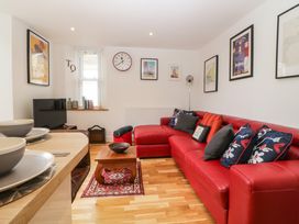 A living room with a red sectional sofa with cushions a wooden coffee table a patterned rug a wall clock framed pictures a television and a dining counter with bowls at Apartment 4 10 Somers Court in Paignton