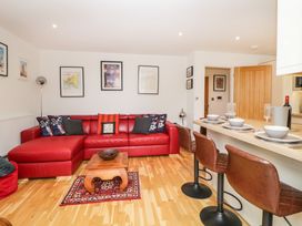 A living room with a red sectional sofa and wooden coffee table beside a kitchen counter with brown bar stools set with dishes at Apartment 4 10 Somers Court in Paignton