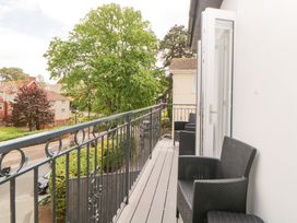 A balcony with black chairs and iron railing overlooking trees and residential buildings at Apartment 4 10 Somers Court in Paignton