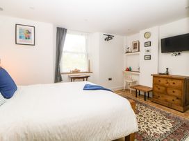 A bedroom with a bed a wooden dresser a wall-mounted television a chair a small table and a window with curtains at Apartment 4 10 Somers Court Paignton