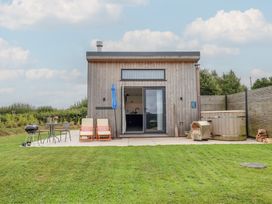 An outdoor area with a wooden building, table, chairs, barbecue and hot tub at The Cadeleigh in Cadeleigh near Tiverton