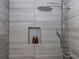 A shower area with a showerhead and products on a shelf at The Pennymoor in Cadeleigh near Tiverton