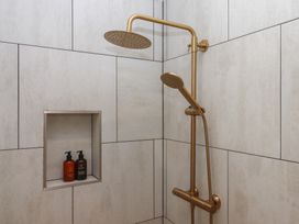 A shower with a gold shower head and niche containing shampoo and conditioner at The Bickleigh Cadeleigh near Tiverton