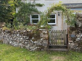 A stone wall with a wooden gate and flowerbed at Greywalls in Maulds Meaburn