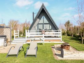A small A-frame cabin with a porch two lounge chairs a picnic bench and a fire pit in the garden at Buttercup Lodge in Misterton
