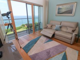 A living room with a beige recliner sofa a colorful geometric rug a telescope and a balcony overlooking the sea at Elanora in Carbis Bay