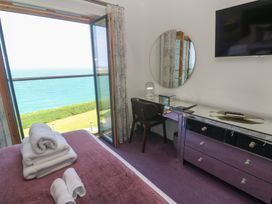 A bedroom with a bed with towels a desk and chair a round mirror a dresser and a wall mounted TV overlooking the sea at Elanora in Carbis Bay