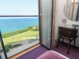 A bedroom with an open door leading to a balcony overlooking the sea a chair and a dressing table with a round mirror at Elanora in Carbis Bay