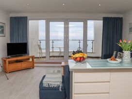 A living room with a television on a wooden stand and a sofa next to a kitchen island with fruit and flowers at Harbour View in Carbis Bay