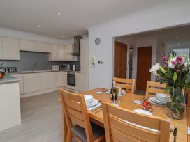 A dining table set with plates bowls utensils and a vase of flowers next to a kitchen with white cabinets and stainless steel appliances at Harbour View in Carbis Bay