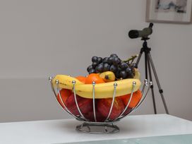 A fruit basket with bananas grapes apples and oranges on a white surface with a telescope in the background