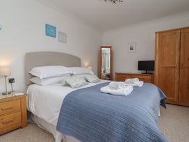 A bedroom with a double bed with blue bedspread two wooden bedside tables lamps wooden wardrobe dresser with tv and standing mirror at Harbour View in Carbis Bay