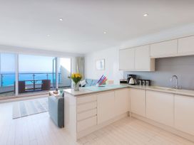 A modern kitchen and living area with white cabinets, a vase of yellow flowers, a light blue sofa, glass doors opening to a balcony with ocean views at Harbour View in Carbis Bay