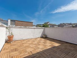 An outdoor terrace with wooden tile flooring two potted plants and white walls with neighboring houses visible Harbour View Carbis Bay